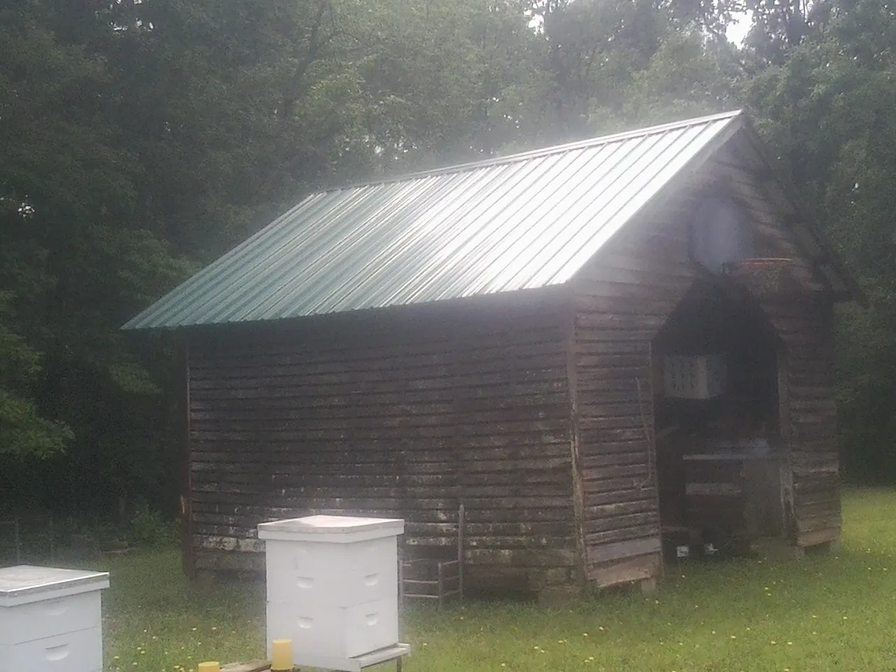 Green metal roof on a weathered barn beside stacked beehives in Newburg